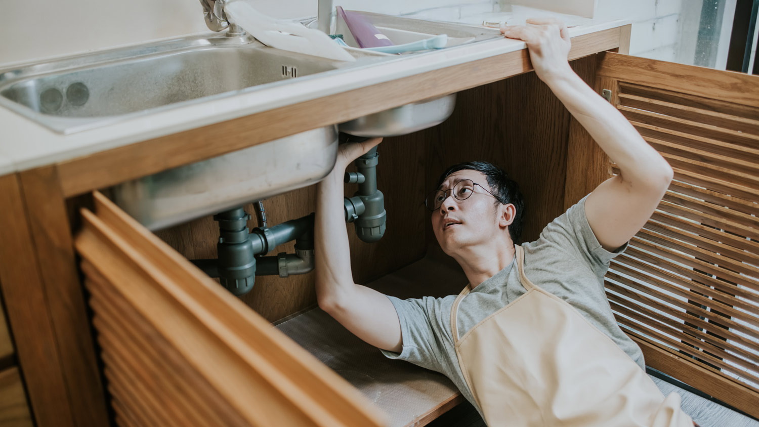 A man fixing pipes under a sink