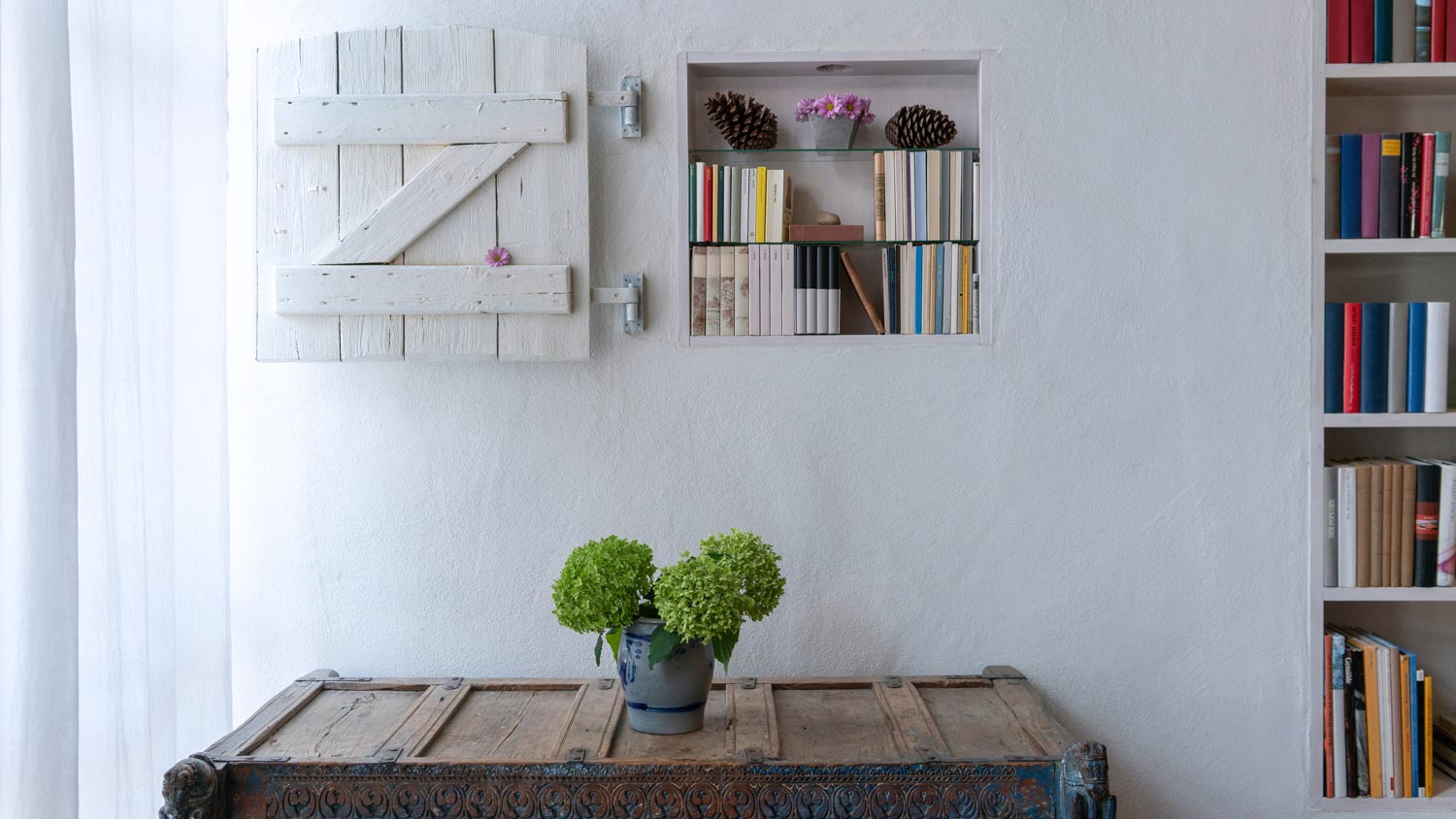 A vase with flowers beneath a recessed within the wall bookshelf