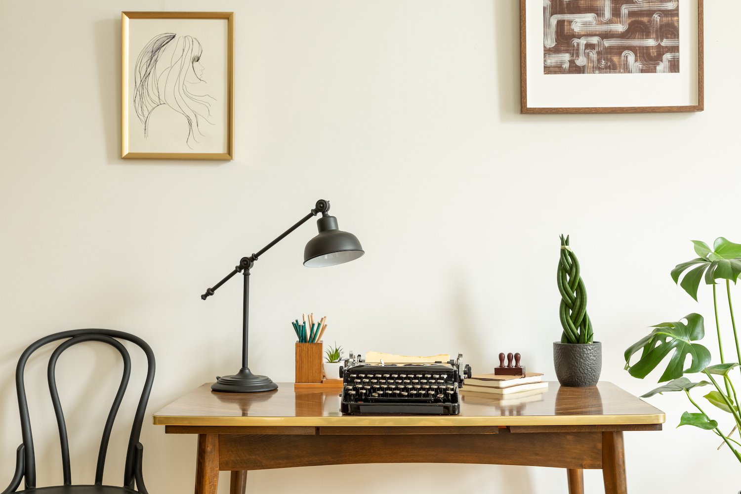 Minimalist home office with an antique wooden desk with a black desk lamp, pencil holder, vintage typewriter and plants