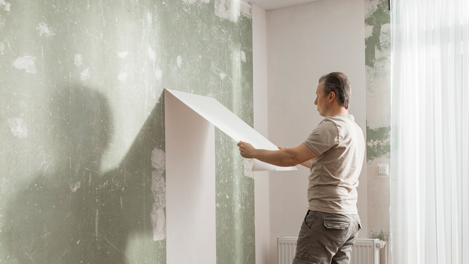 Man peeling off old wallpaper from wall in living room at home