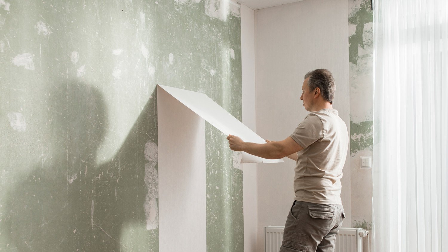 Man peeling off old wallpaper from wall in living room at home  