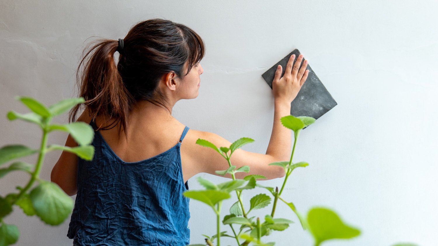 Woman Repairs White Wall Using Sandpaper