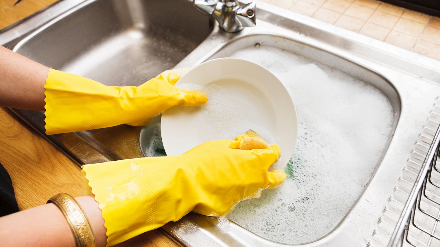 Woman wearing rubber gloves washing dishes in a compartment sink