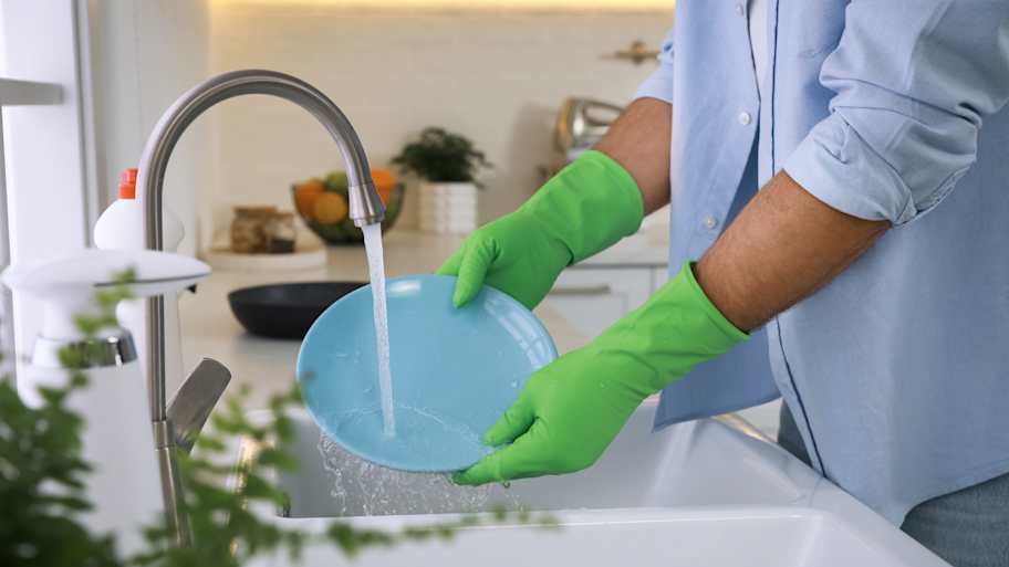 A man wearing rubber gloves washes dishes in the kitchen sink