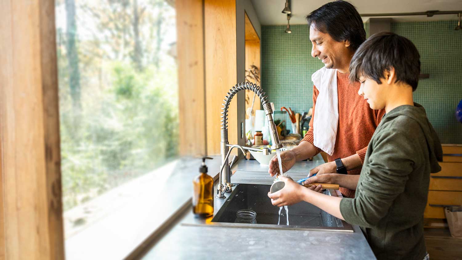 Father and son washing dishes in the kitchen sink