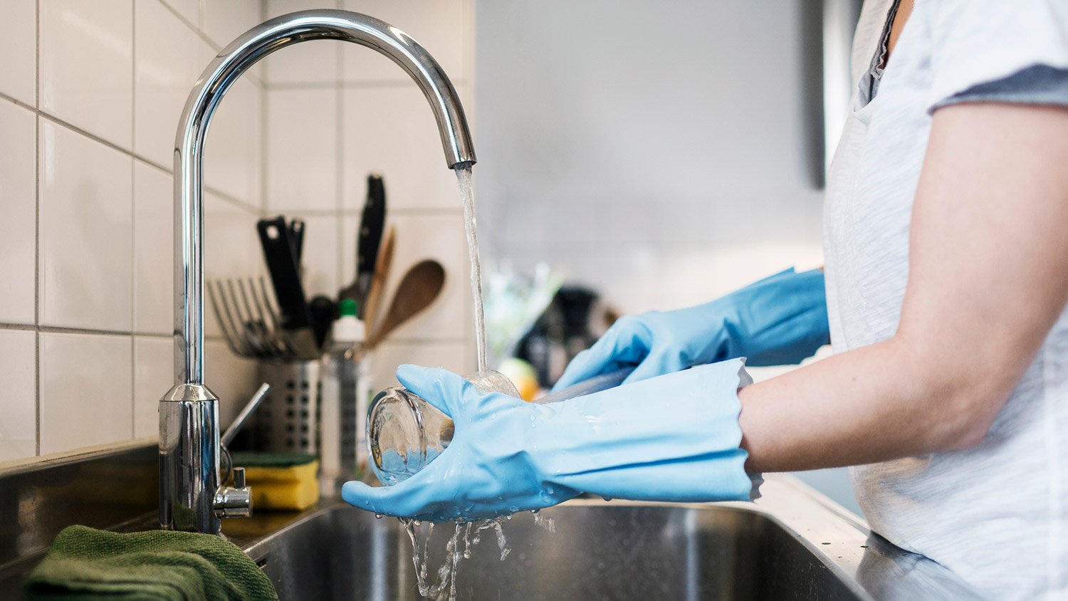 Woman washing glass at stainless steel sink in kitchen