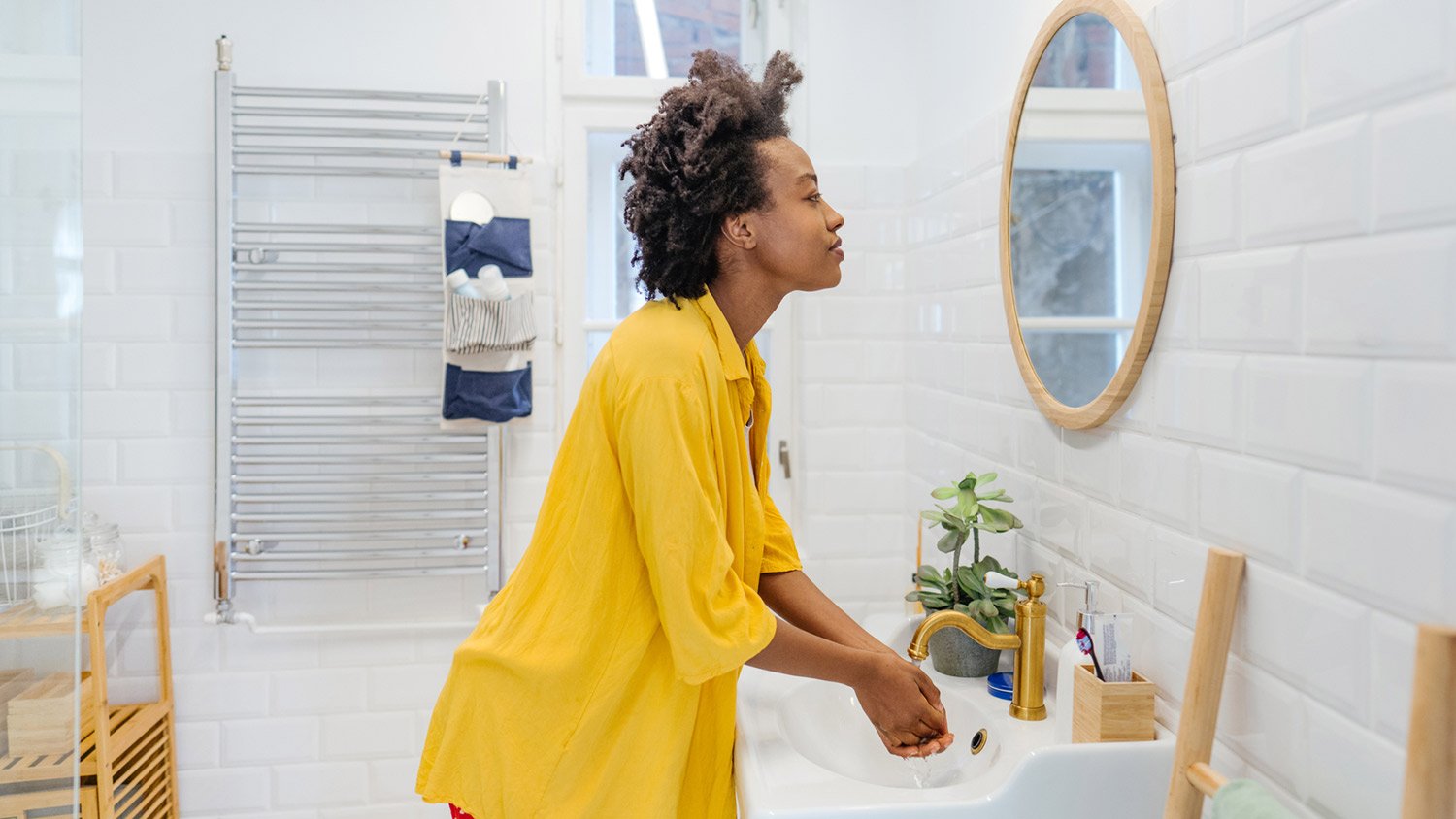 Woman washes hands in bathroom sink while looking in mirror