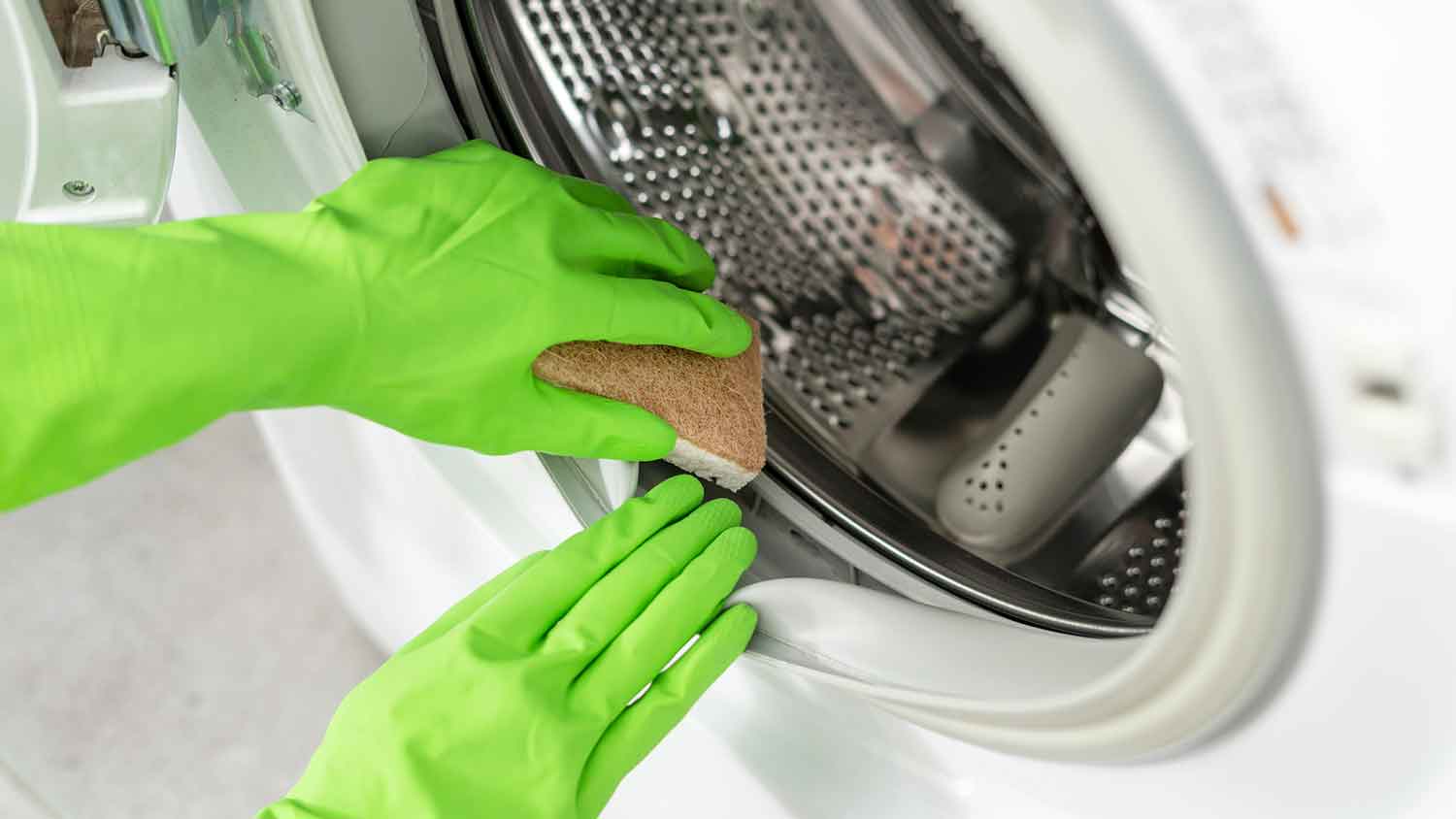 Person wearing gloves cleaning washing machine door gasket 