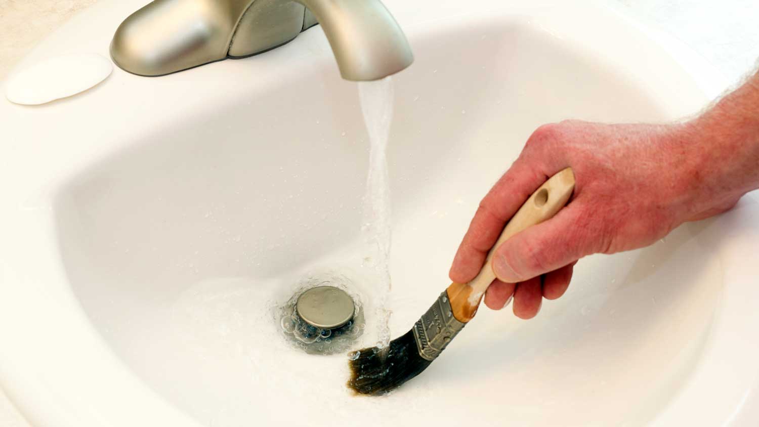 Man washing a paintbrush in the bathroom sink