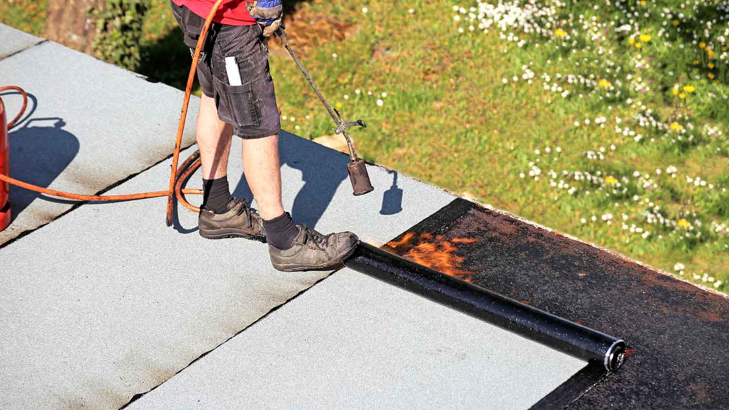 Worker waterproofing flat roof with bitumen membranes 