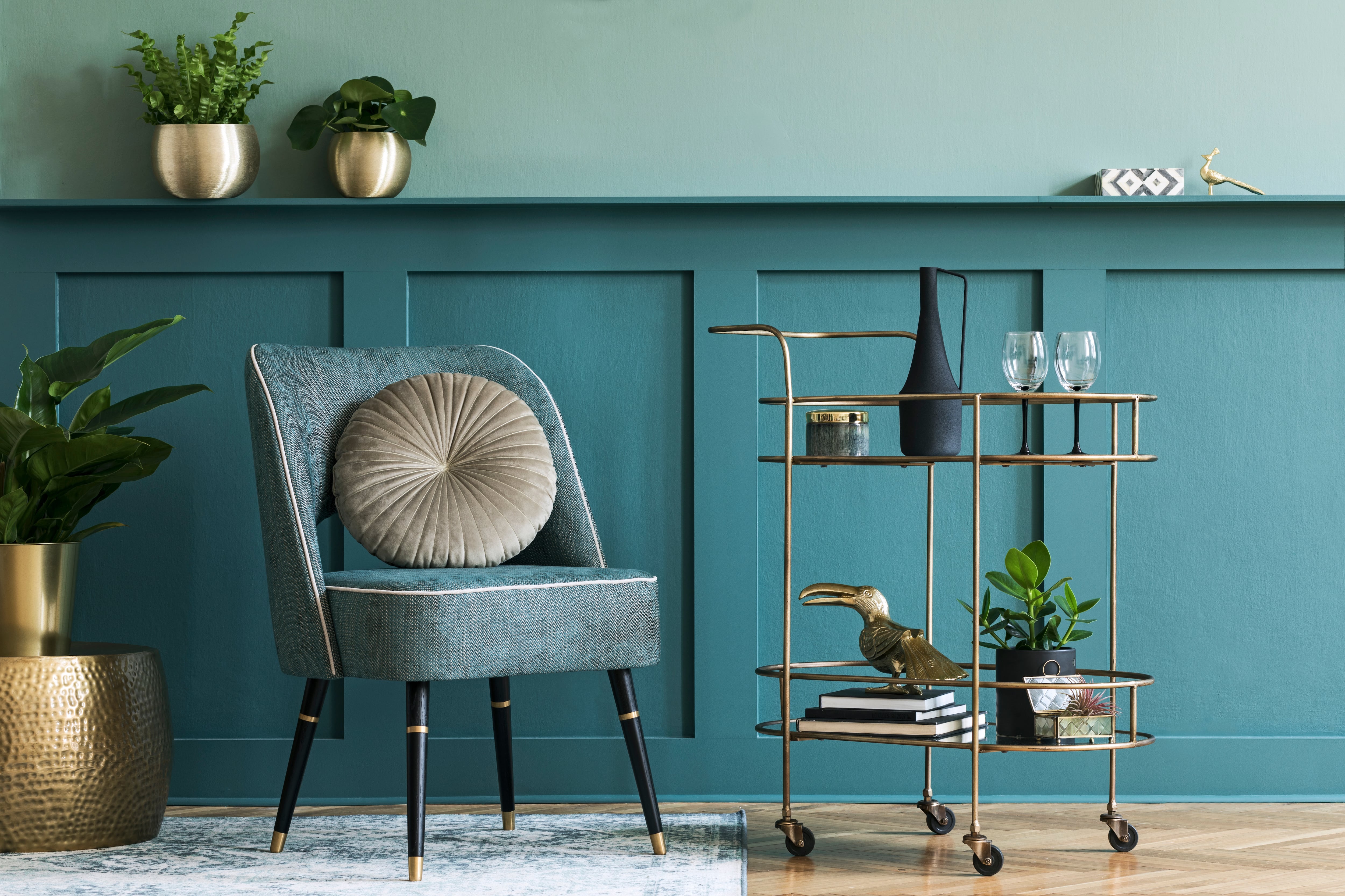 A teal room with a chair and a gold bar cart