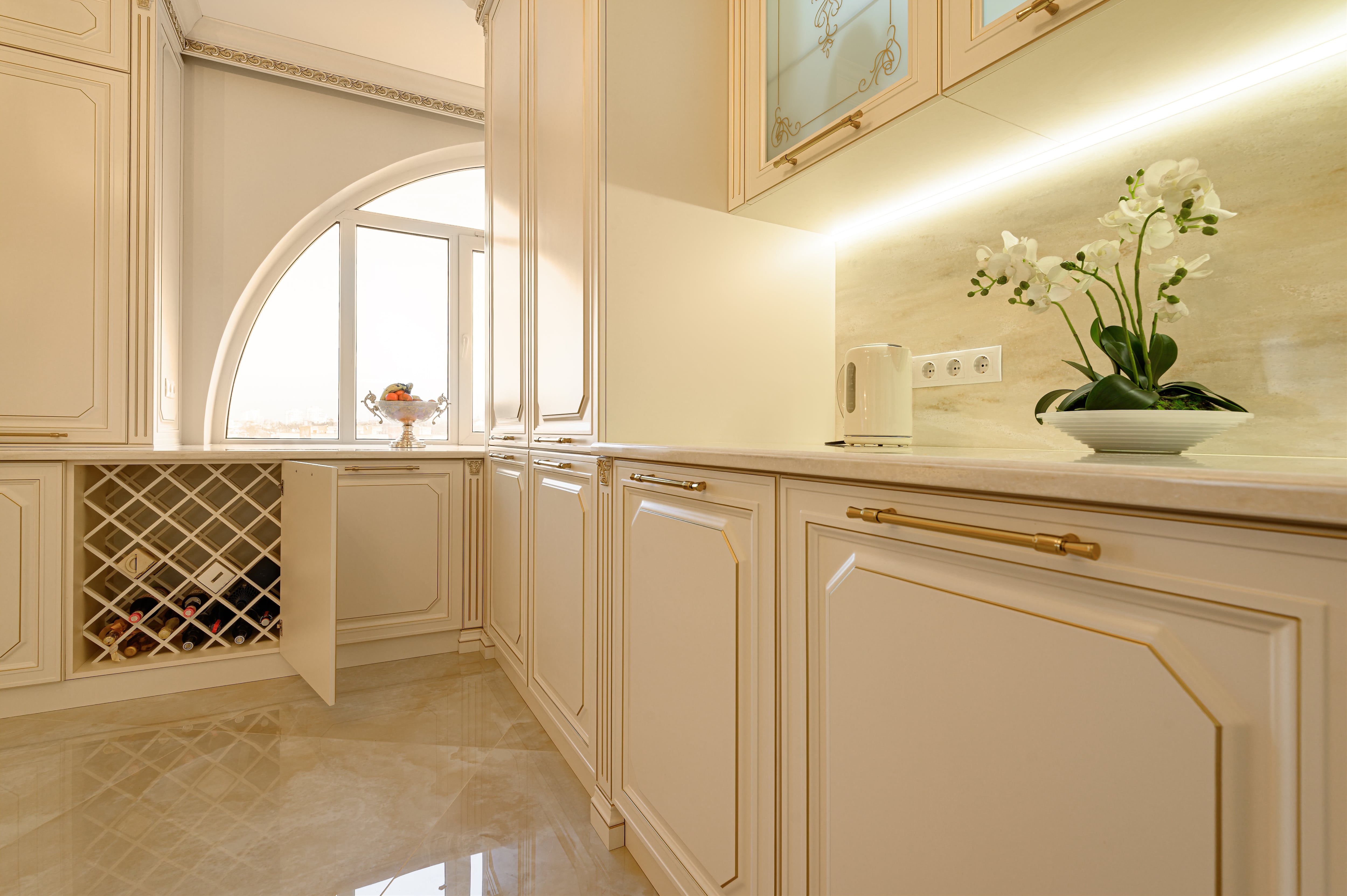 A gold and off-white kitchen with open wine storage cabinet