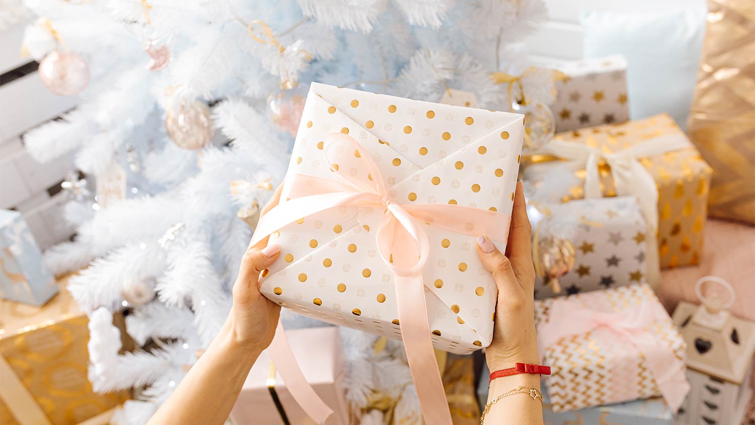 woman holding gift next to white christmas tree 