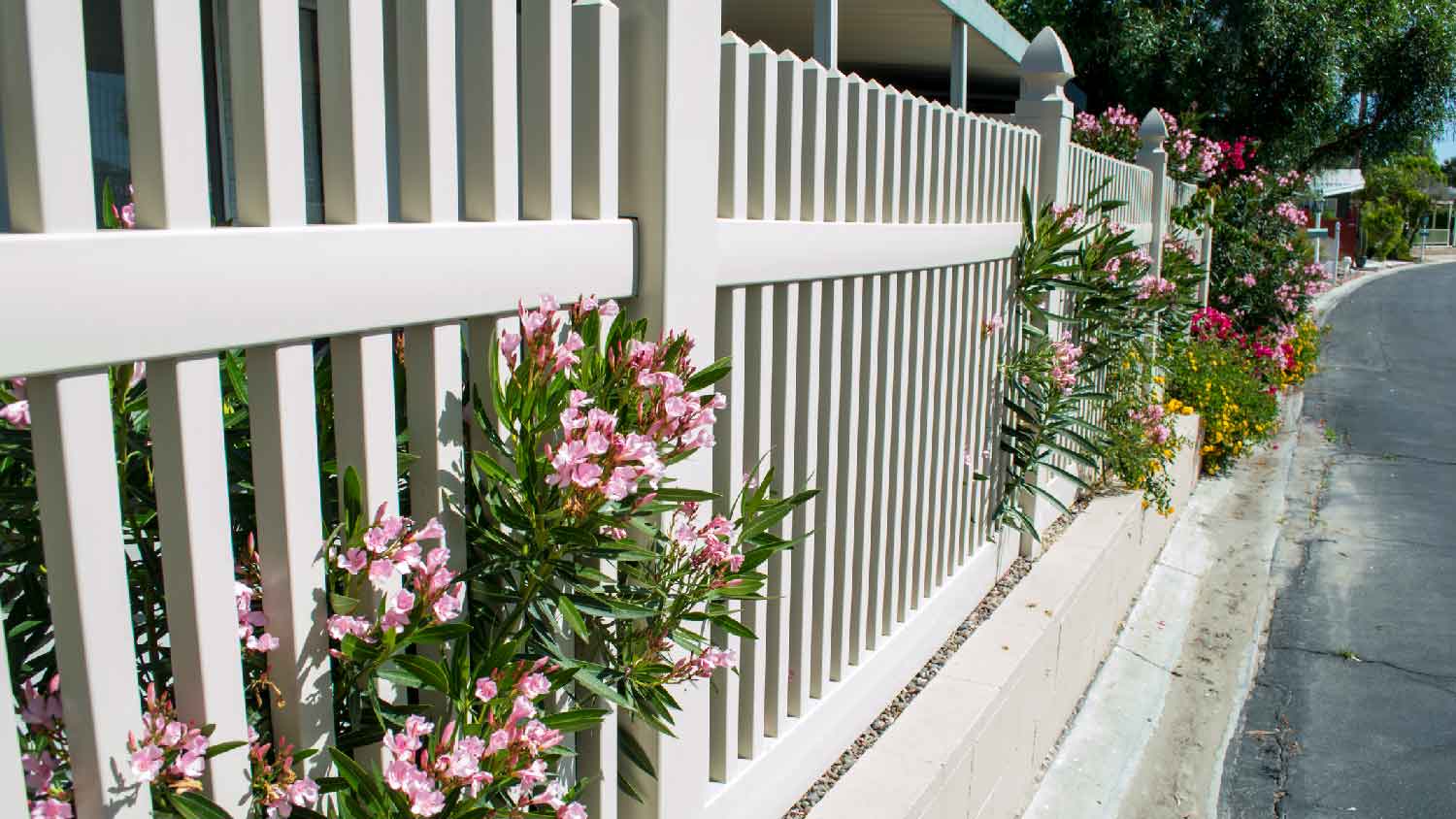 A white vinyl picket fence with flowers sticking through the pickets