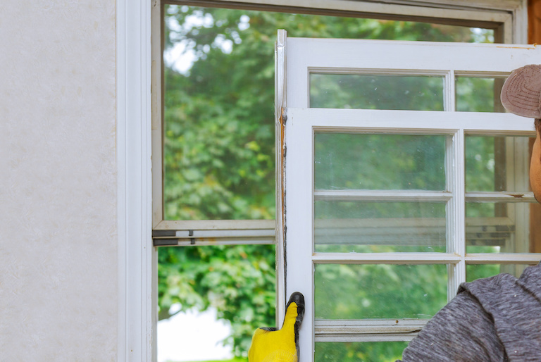 yellow-gloved hands hold windows in front of empty window frame for repair