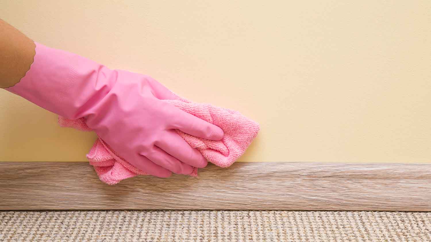 Woman wearing rubber gloves wiping interior wall with a microfiber cloth