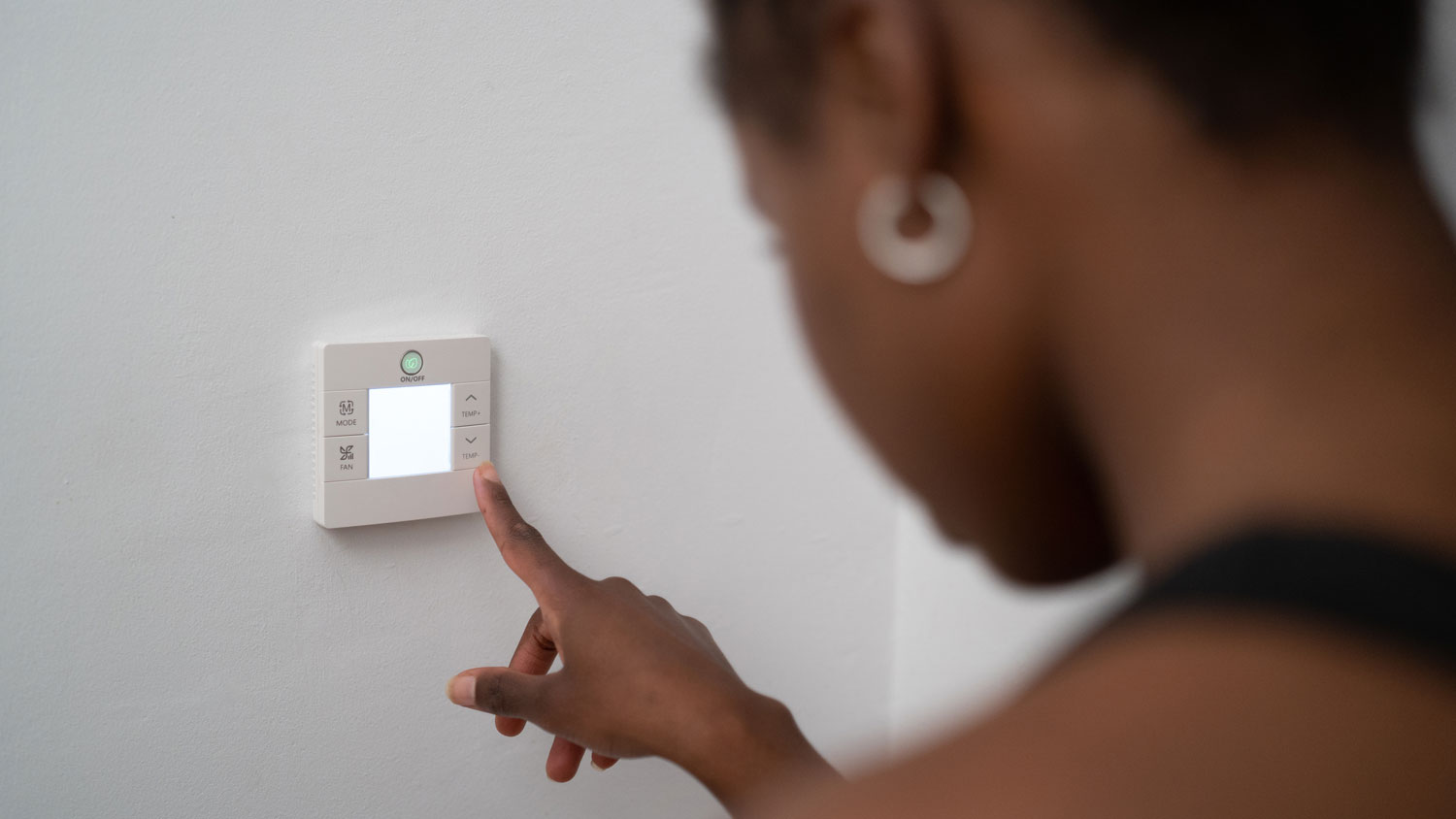 A woman adjusting the temperature via a thermostat