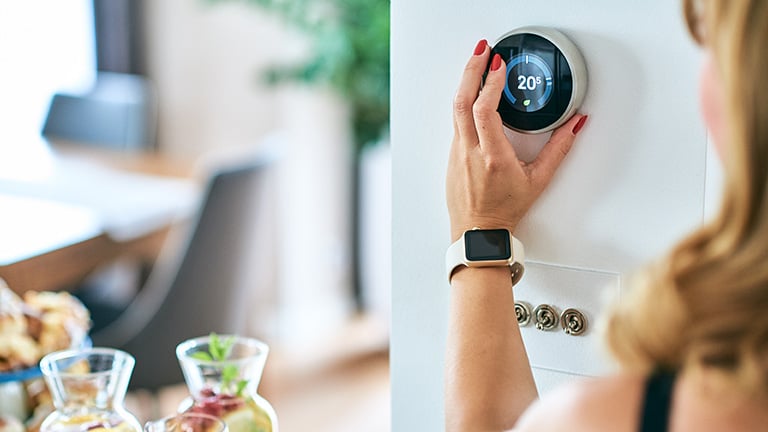 Woman adjusts air-conditioner’s temperature via a digital thermostat