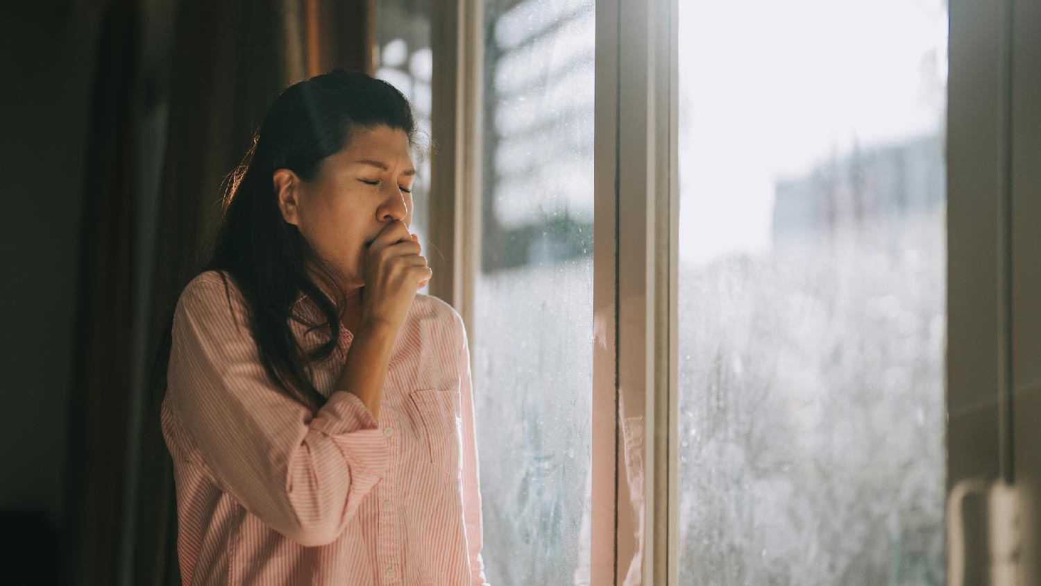 A woman with allergies sneezing by the window