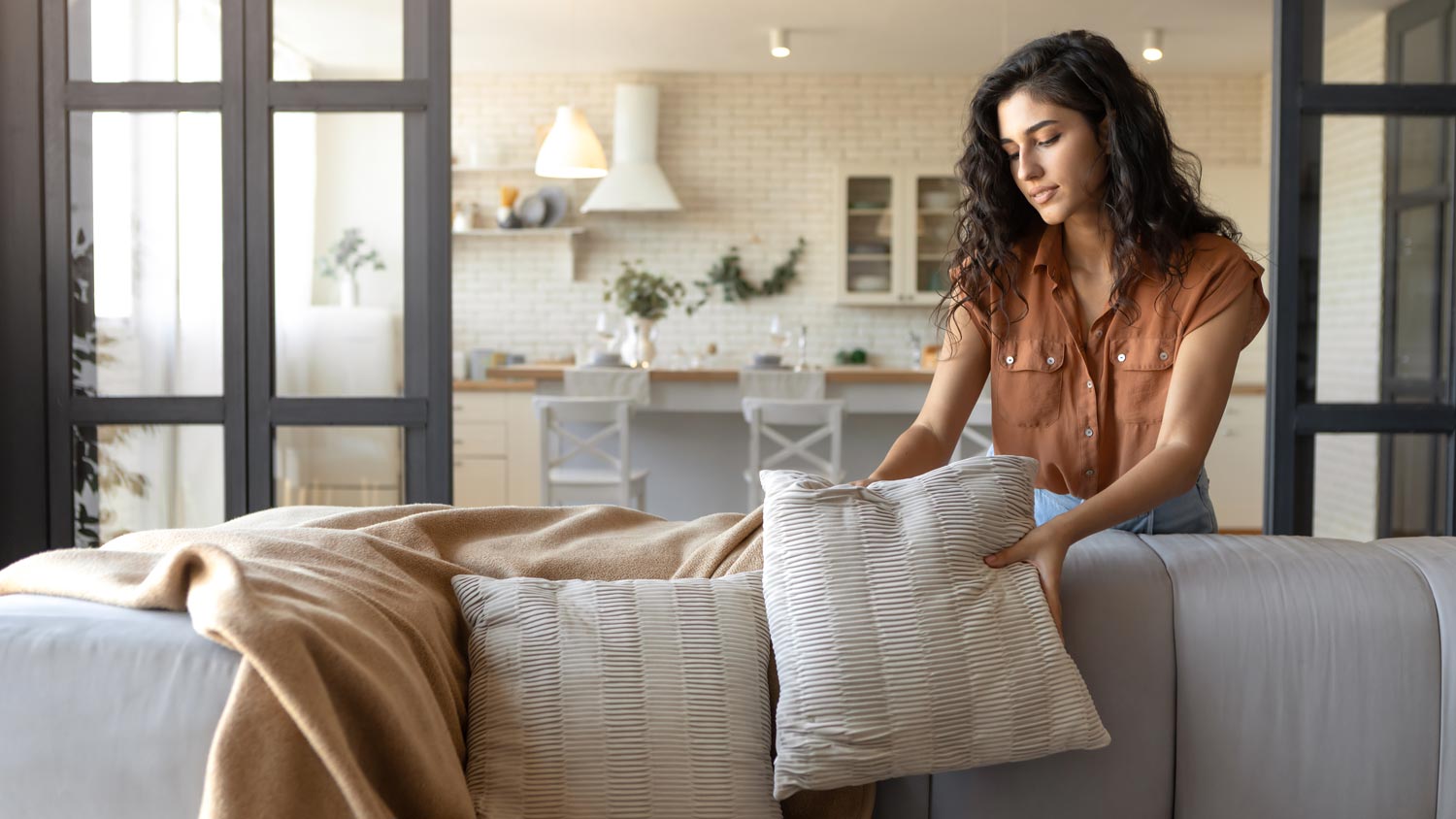 A young woman arranging pillows and a plaid on a sofa