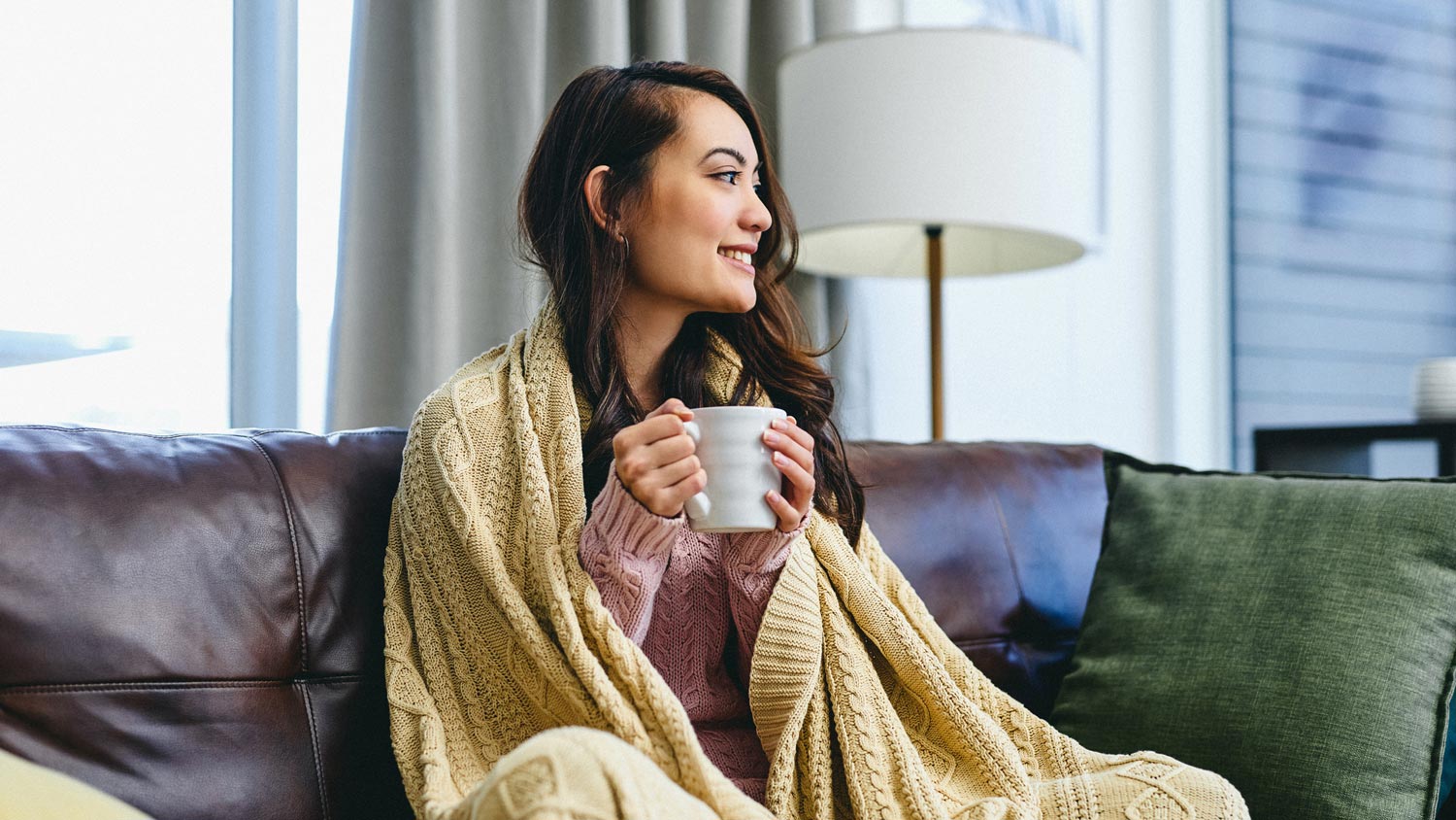 A woman covered in a blanket drinking some coffee