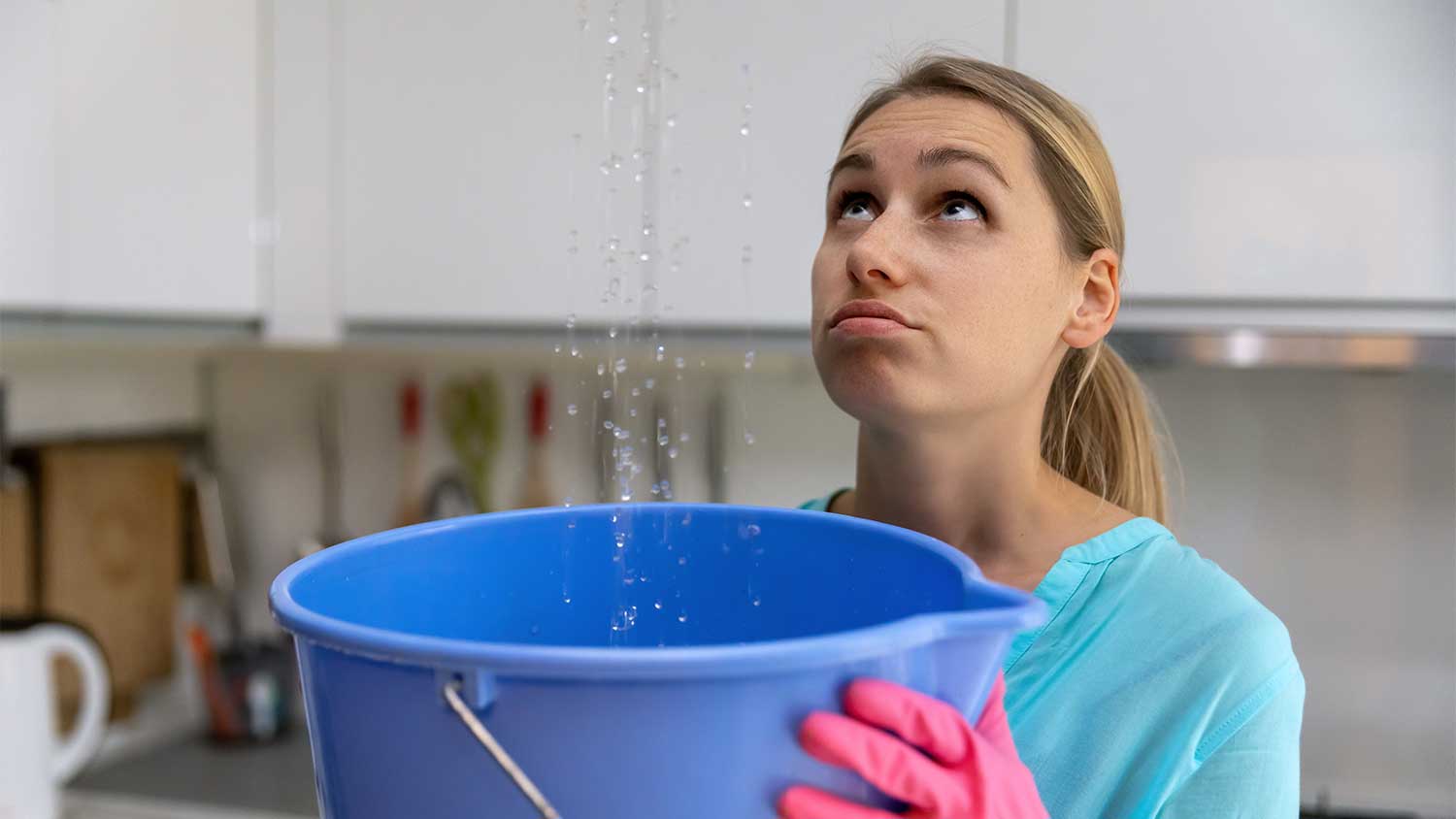 A woman catches water from a leak in a bucket