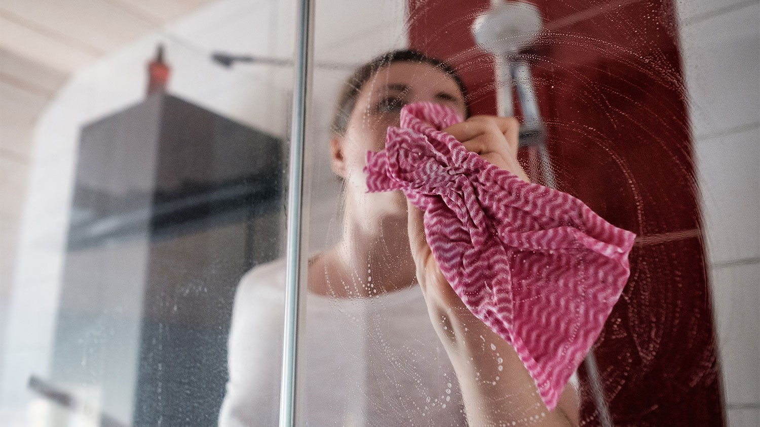 A woman cleans a glass shower door