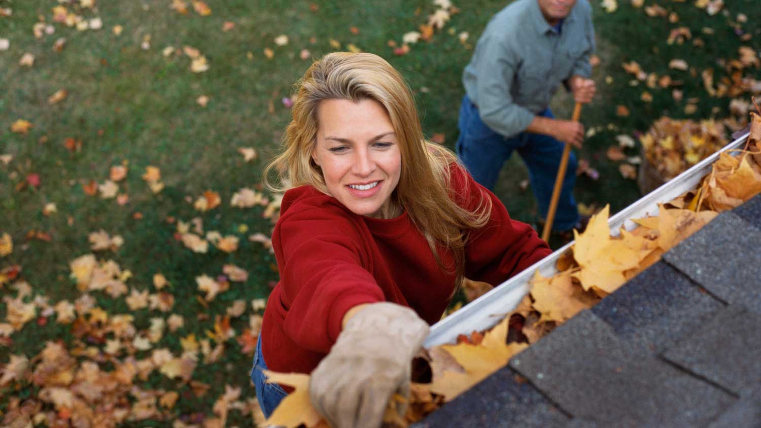 A woman cleaning the gutter from autumn leaves