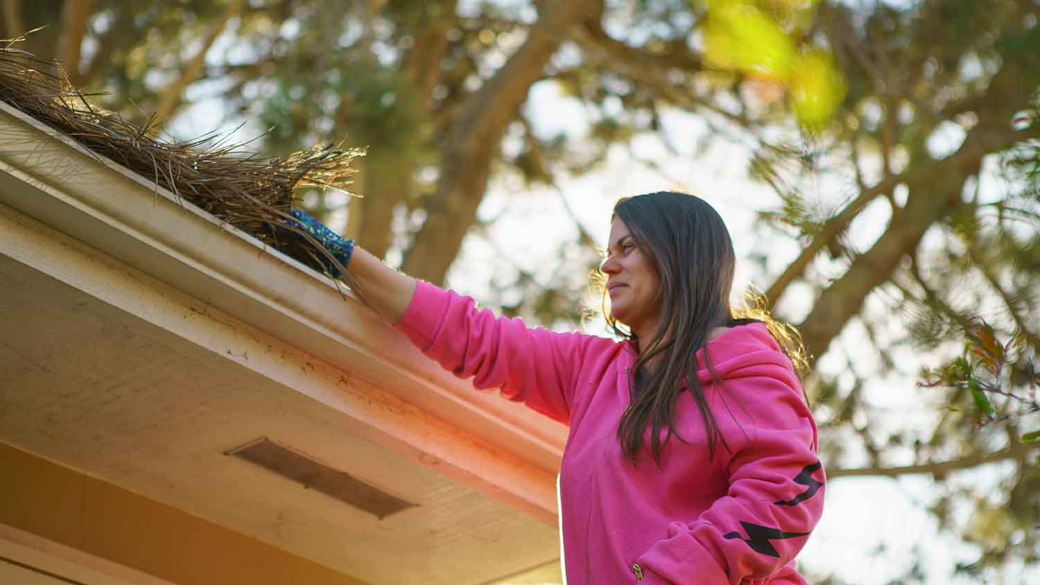 Woman on a ladder cleaning the gutters of the house