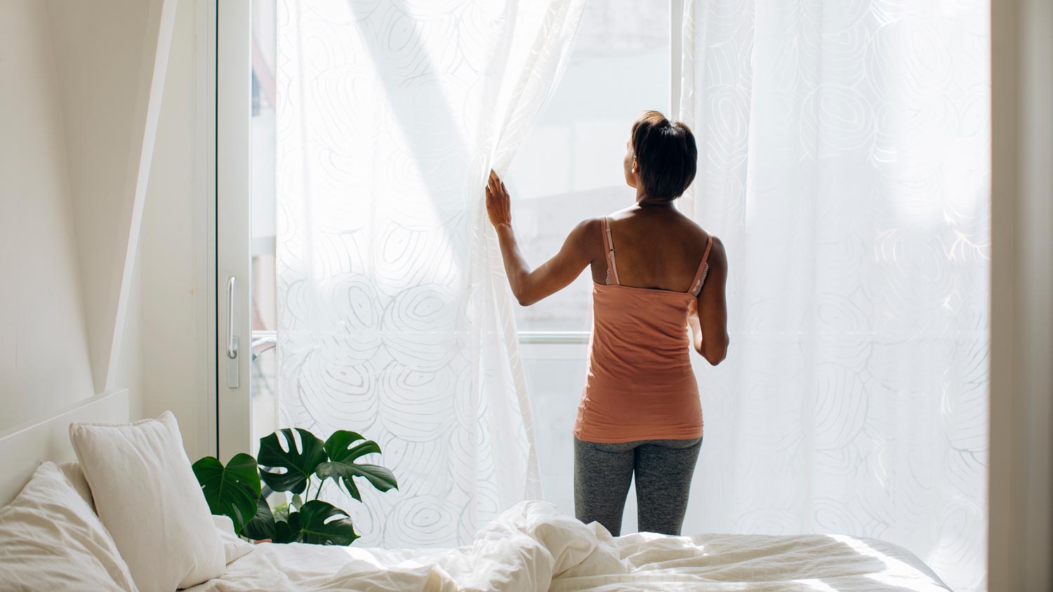 A woman closing the drapes to block the sun