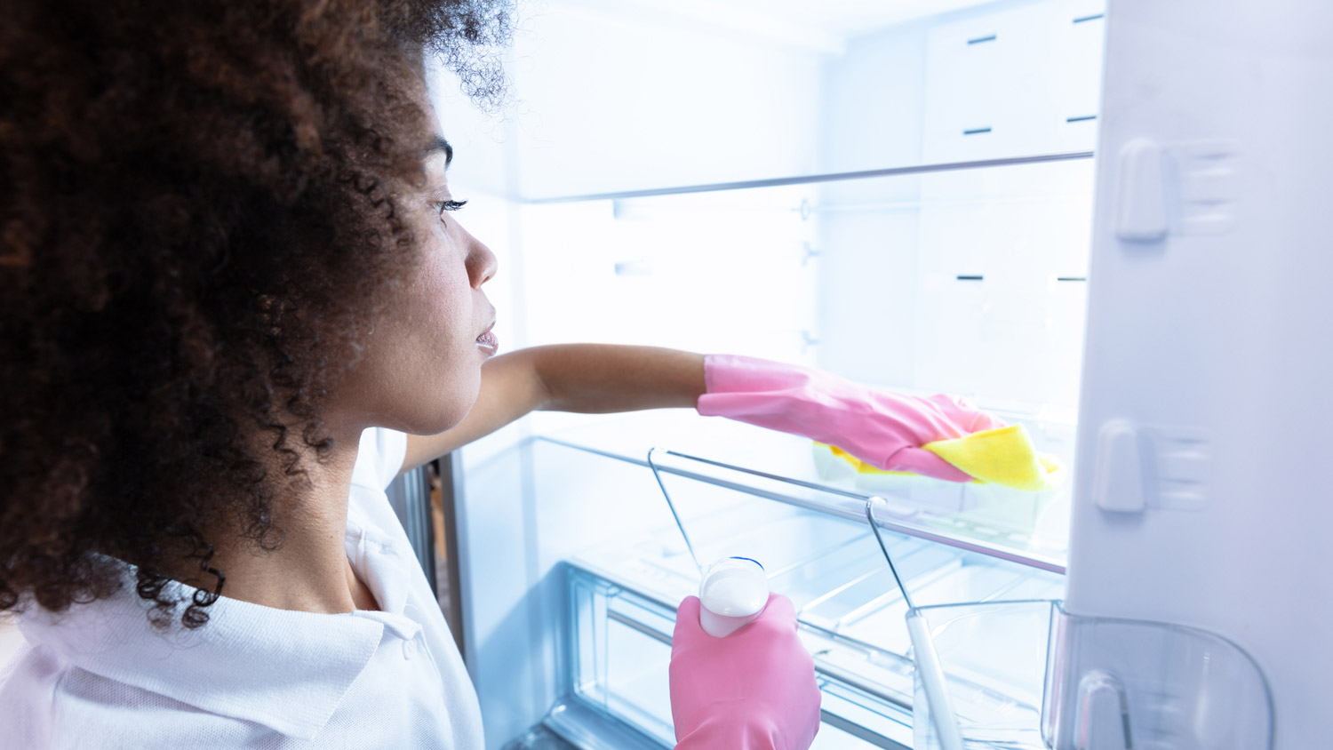 A woman in protective gloves cleaning the fridge