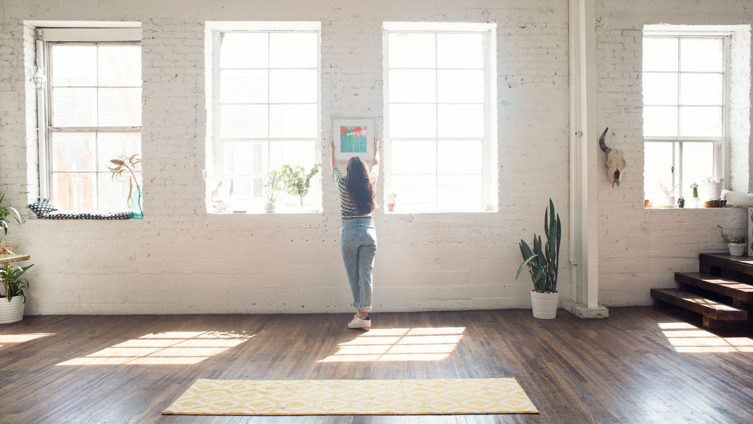 A woman hanging art to brick wall in her loft