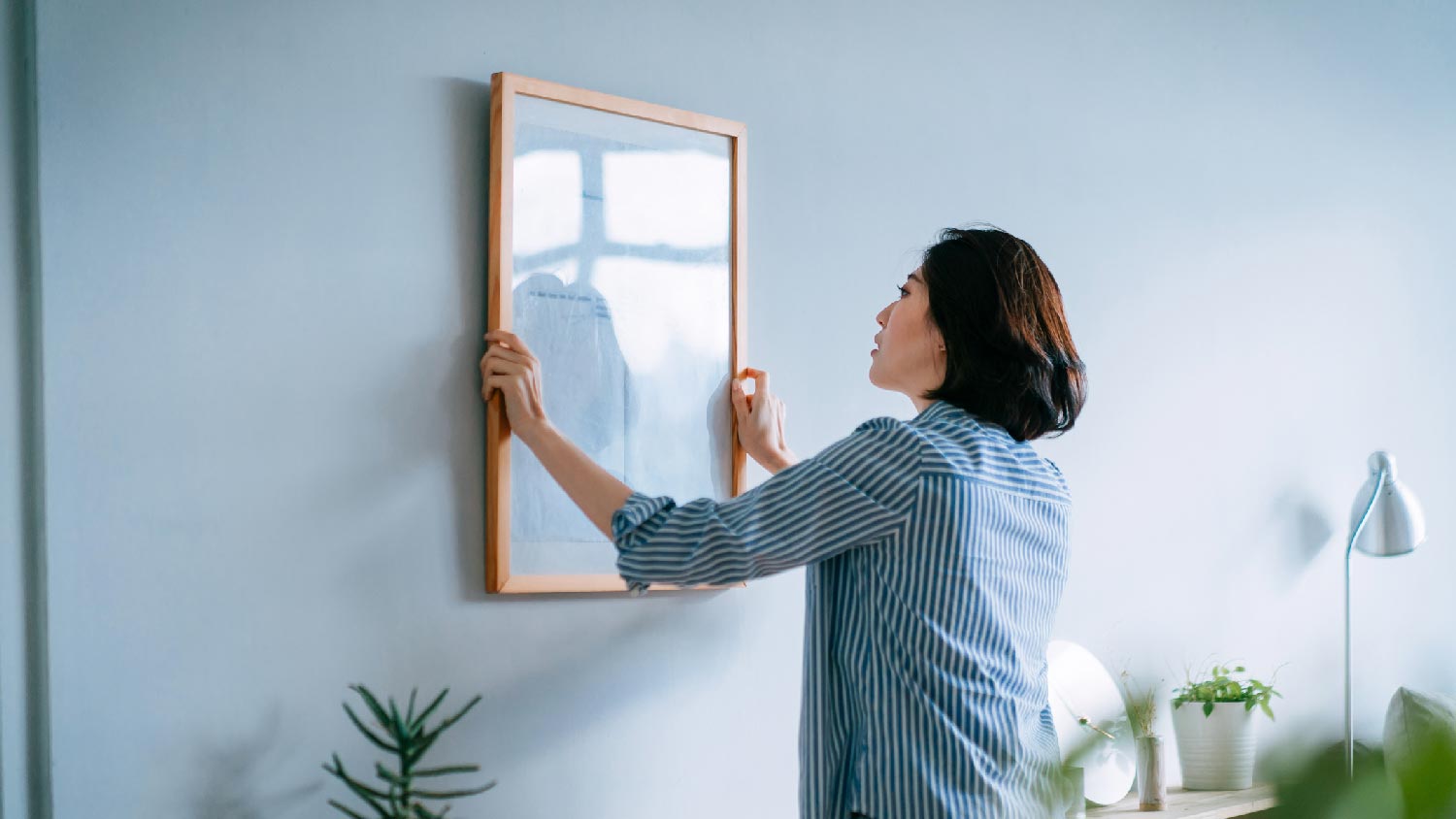 A woman hanging a picture on a drywall