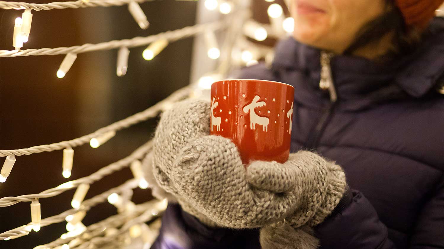 A woman holds a mug and looks at LED Christmas lights