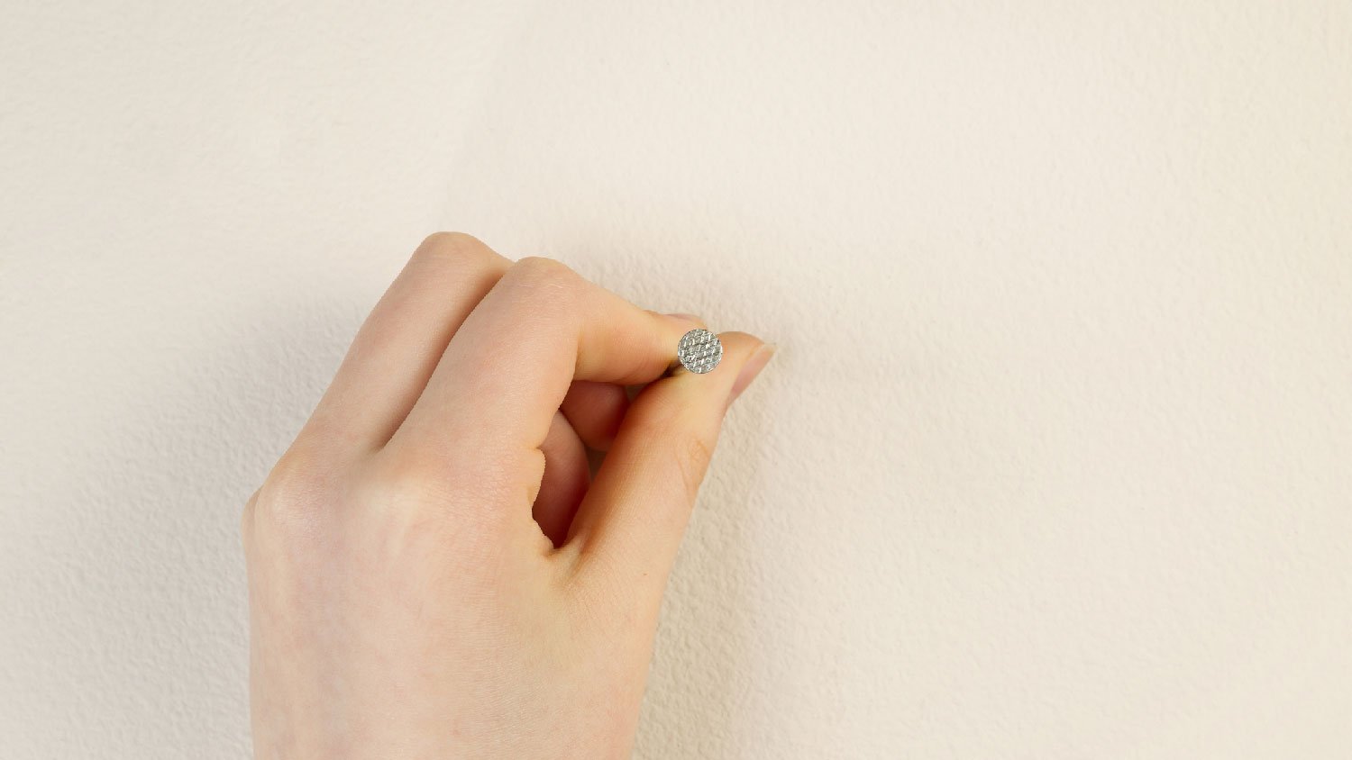 A woman holding a nail against a drywall