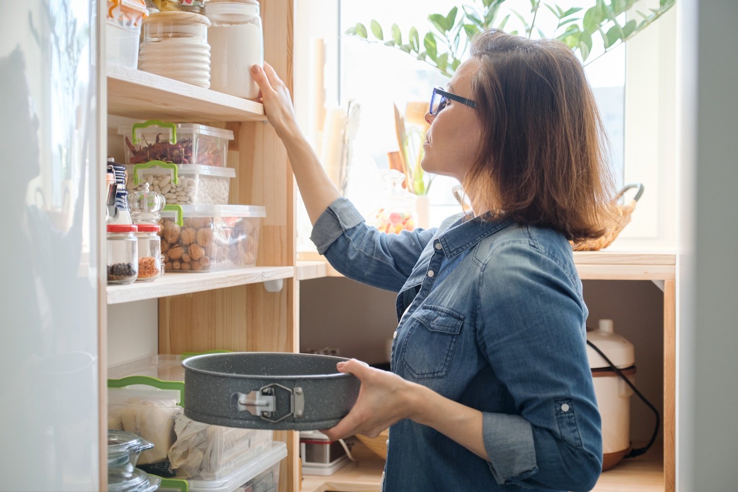 Woman holding a pan and taking flour out of her kitchen pantry