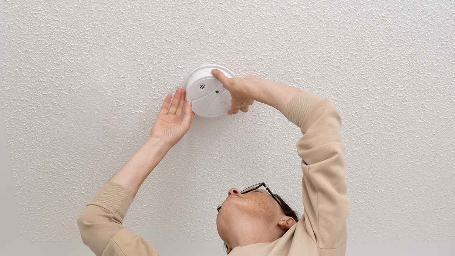 Woman installing smoke detector on the ceiling