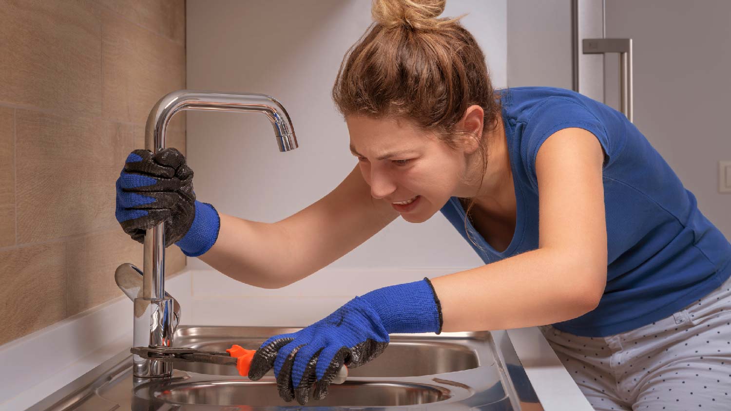 A woman maintaining a kitchen faucet by tightening the mounting bolts