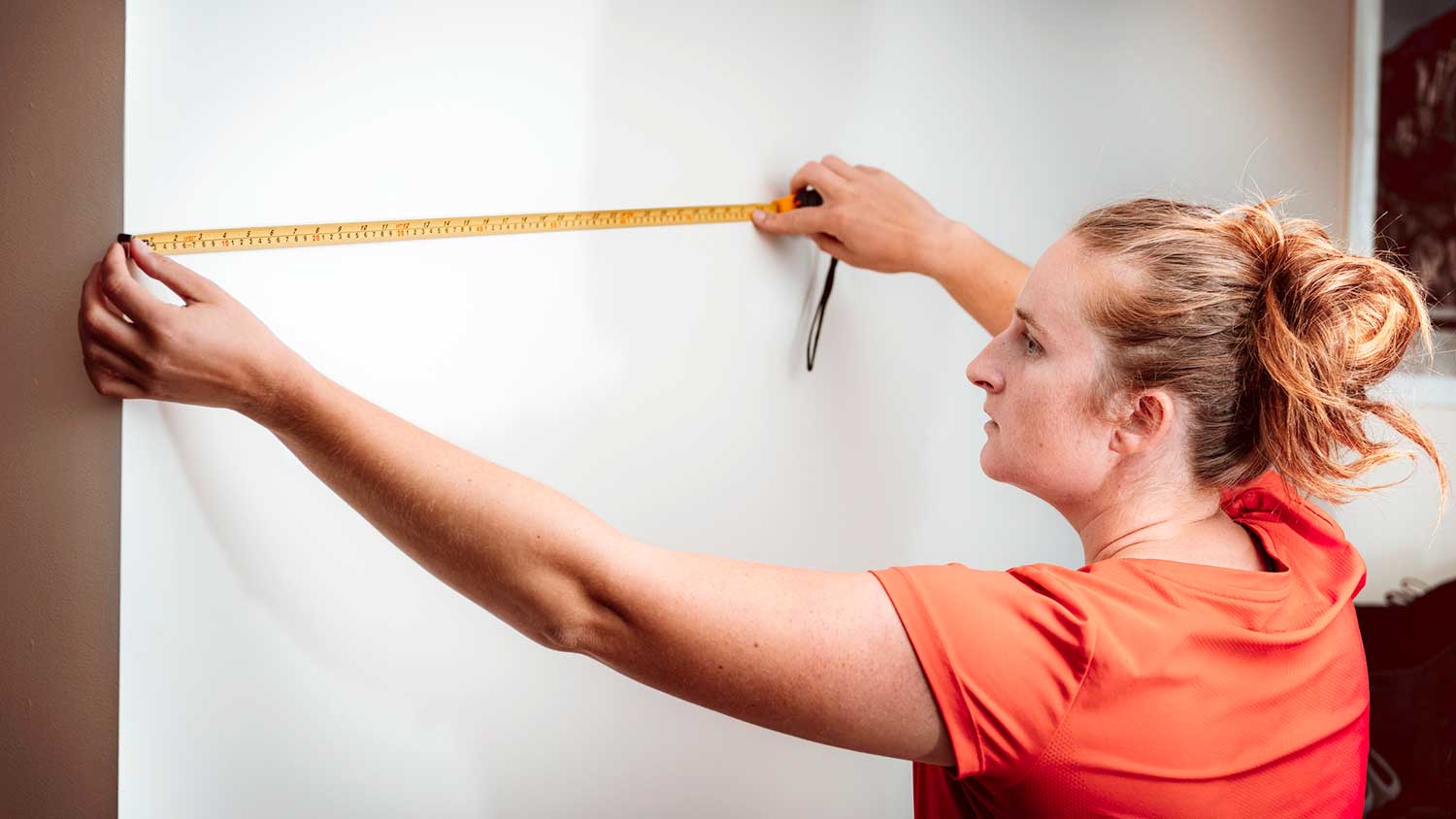 Woman using measuring tape to measure interior wall 