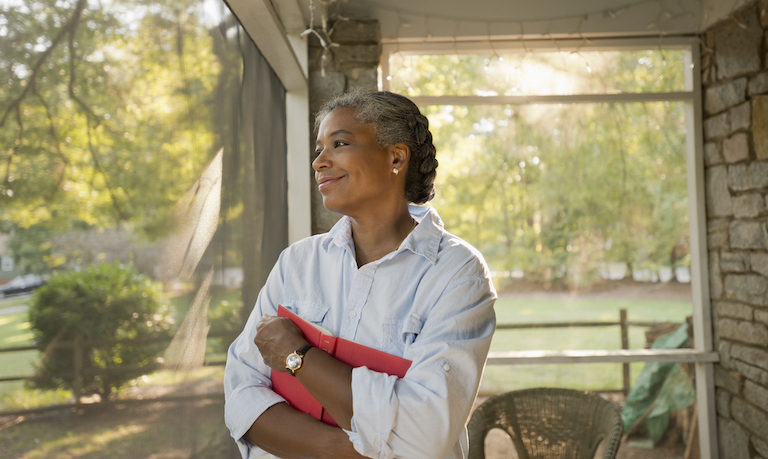 woman holds book and smiles on screened in porch