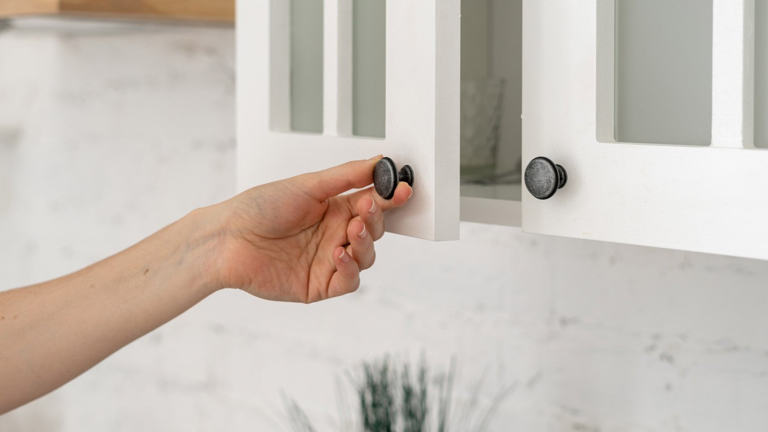 A woman opening a kitchen cabinet by the knob