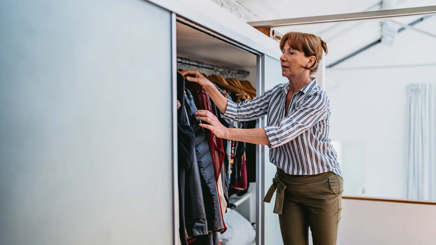 woman opening a closet to grab hanging clothes 