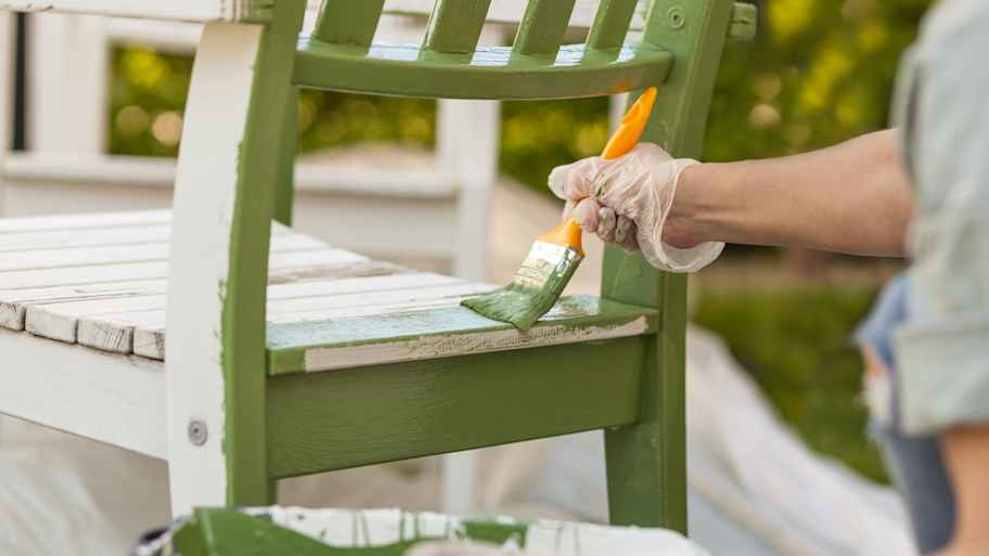 A woman painting a chair in olive green with a brush
