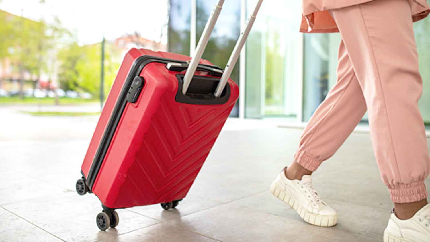 Woman leaving the airport is pulling a red wheeled suitcase
