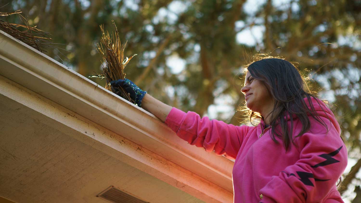 A woman removing debris from gutters