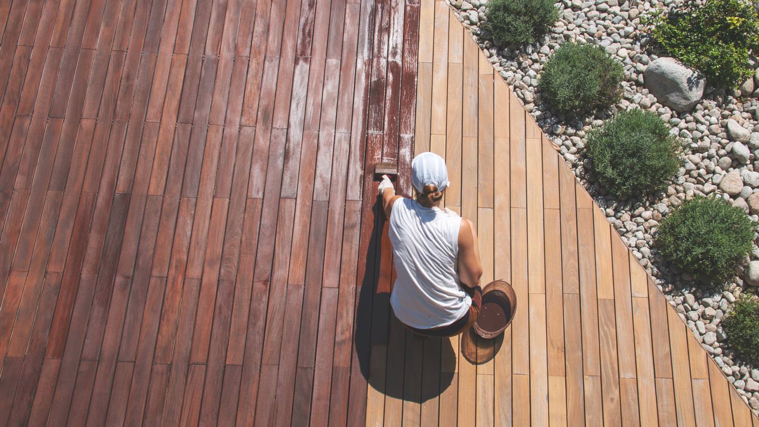 A woman renovating a deck by applying protective wood stain