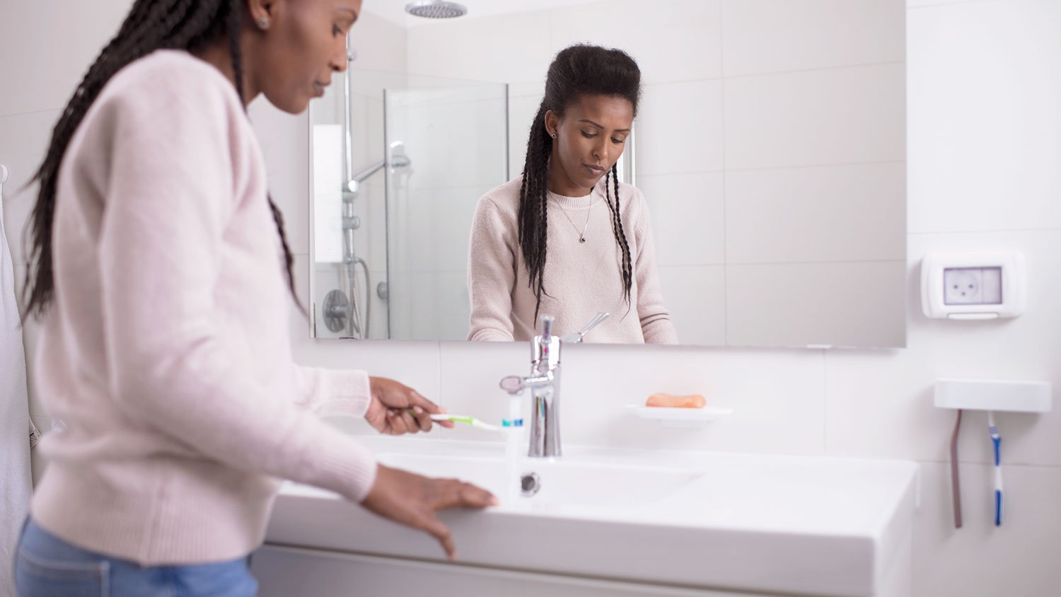 Woman wearing pink sweater rinsing her toothbrush in the bathroom