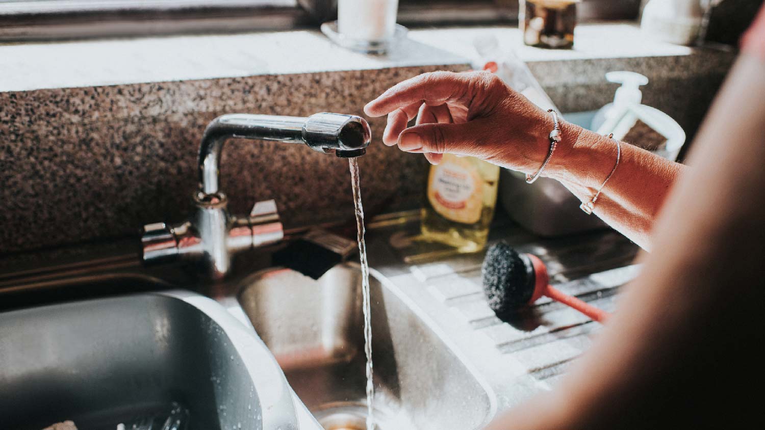 A woman touching running water from faucet