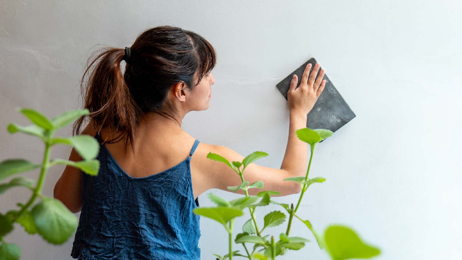 A woman sanding the paint of a wall