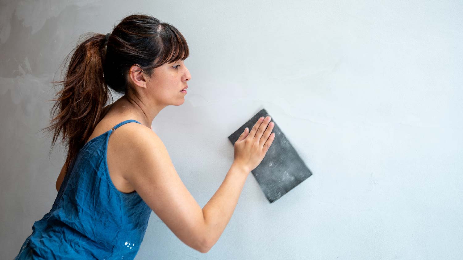 A woman sanding a wall 
